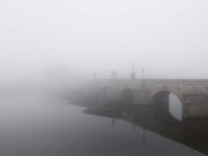 This atmospheric print captures the ethereal beauty of Pisek’s ancient stone bridge, vanishing poetically into a dense fog, creating a surreal and enchanting visual narrative.