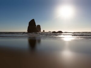 Experience the raw grandeur of Canon Beach, Oregon through this evocative portrayal of dramatic rock monoliths reflecting in the dark, wet sands.