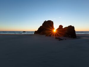 Experience the serene closure of day with this mesmerizing capture, where the Pacific kisses the sun goodbye through dramatic rocky silhouette .