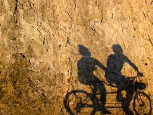 Tranquil synergy of light and shadow, as cyclists cast elongated figures on a sunlit rock wall, epitomizing Vancouver’s vibrant seawall in Stanley Park.