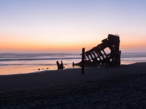 This print encapsulates a haunting yet breathtaking view of the Peter Iredale shipwreck, gloriously silhouetted against a vibrant sunset