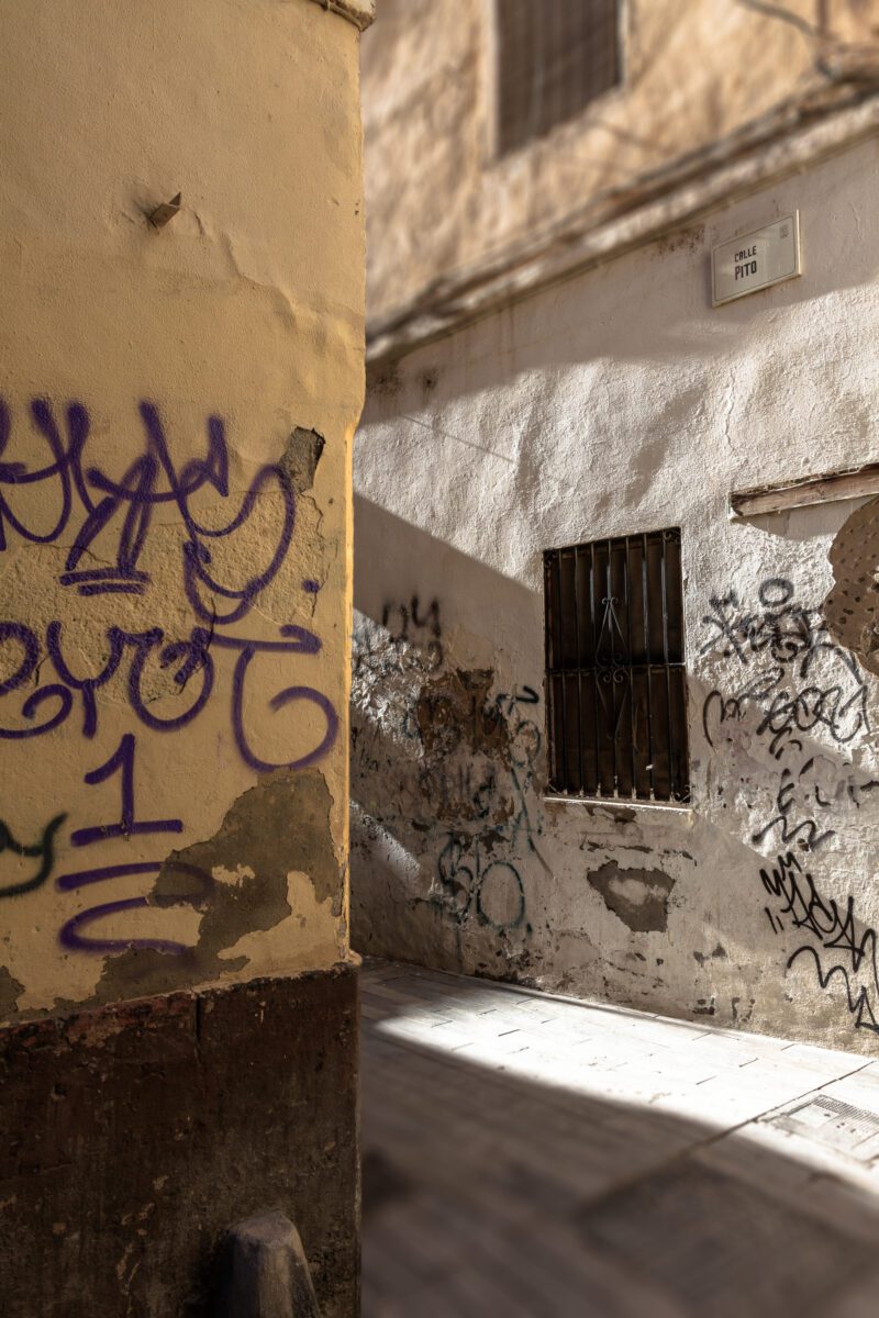 Graffiti-covered walls in a sunlit alleyway of Malaga