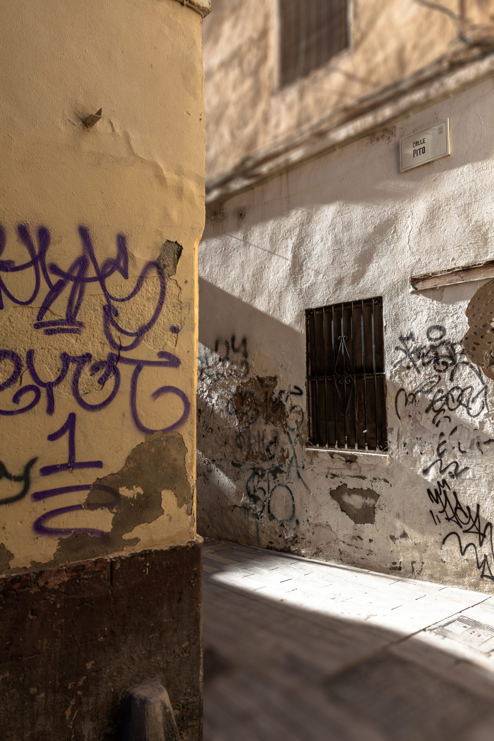 Graffiti-covered walls in a sunlit alleyway of Malaga