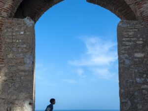 Young boy contemplating under historic Tangier arch with vast ocean background.