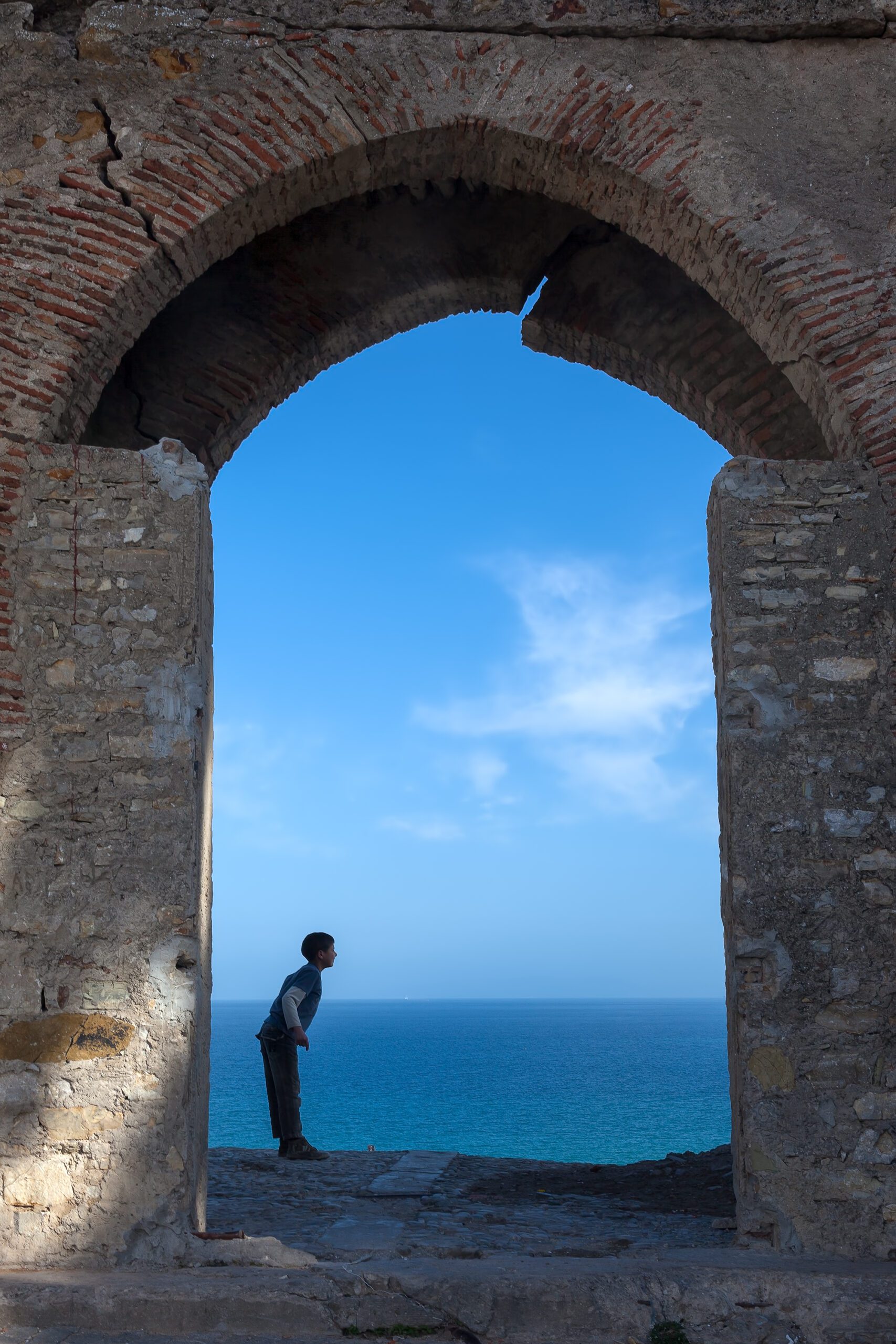 Young boy contemplating under historic Tangier arch with vast ocean background.