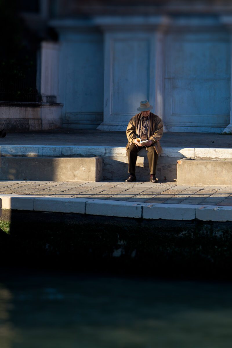 Man sitting by Venice's Grand Canal with historic architecture in the background.