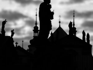 Silhouette of Prague rooftops against a cloudy sky in black and white.