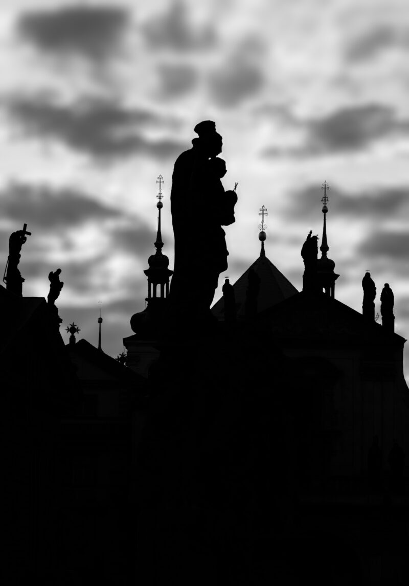 Silhouette of Prague rooftops against a cloudy sky in black and white.