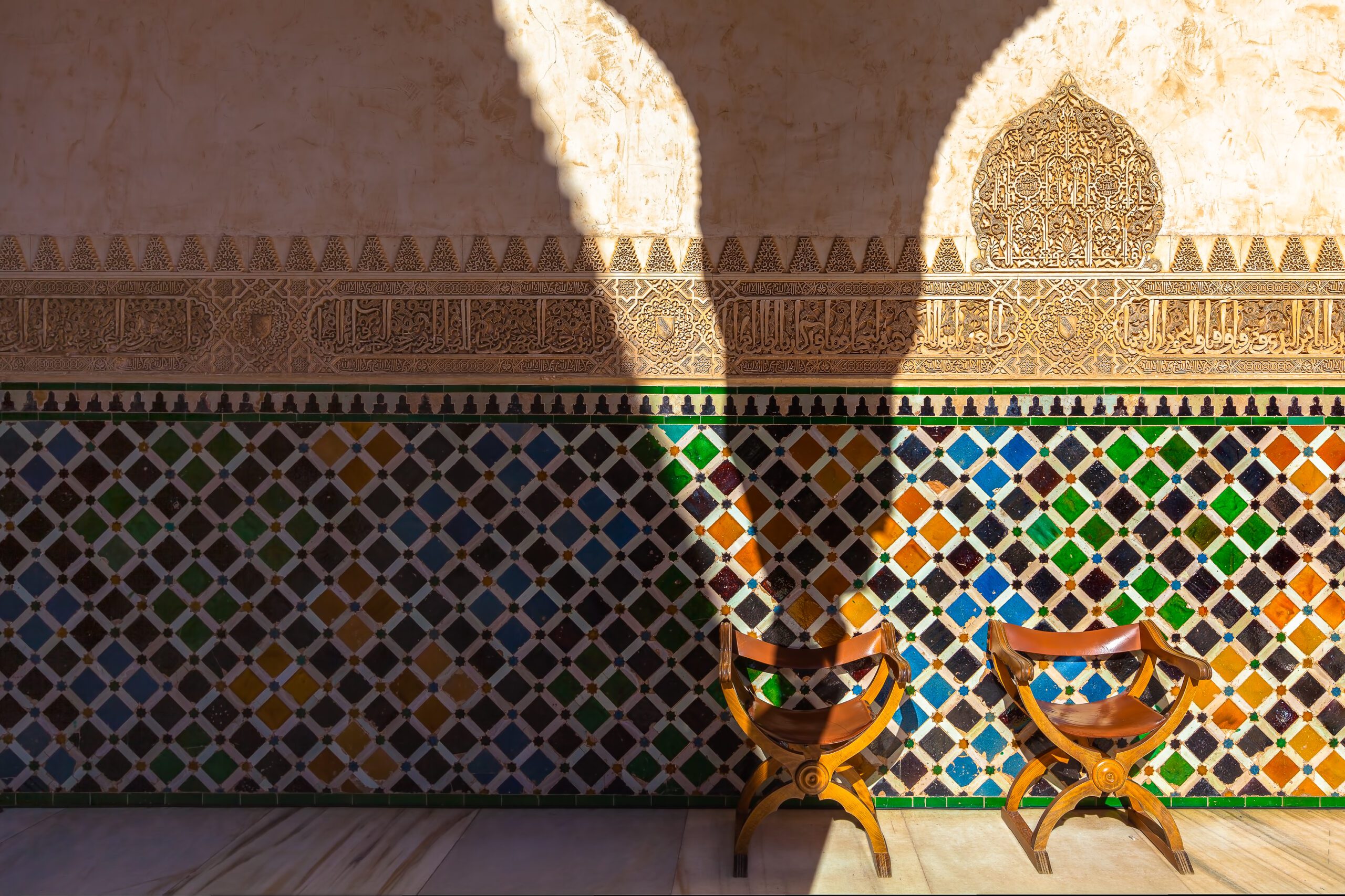 Ornate Alhambra Castle detailing with two wooden chairs in the foreground.