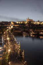 Prague cityscape during twilight with illuminated landmarks and reflections on the Vltava River.