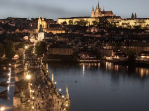 Prague cityscape during twilight with illuminated landmarks and reflections on the Vltava River.