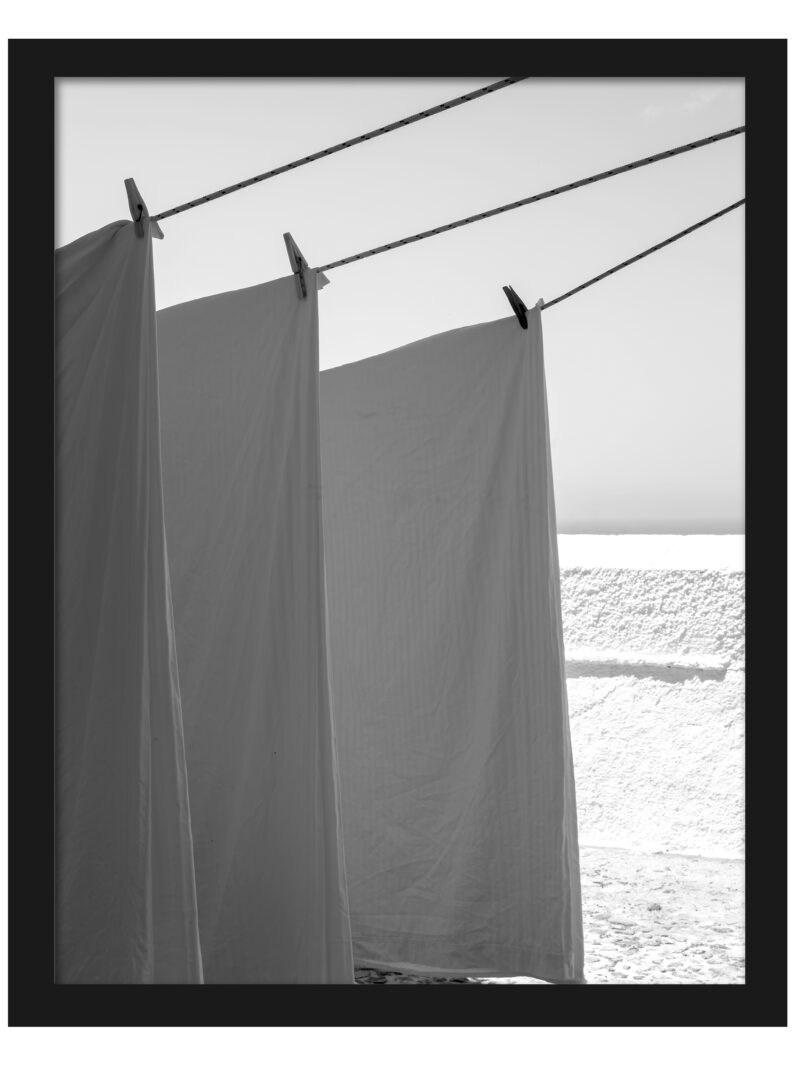 White sheets billowing in the wind resembling sails, set against a bright background in Fira, Santorini.