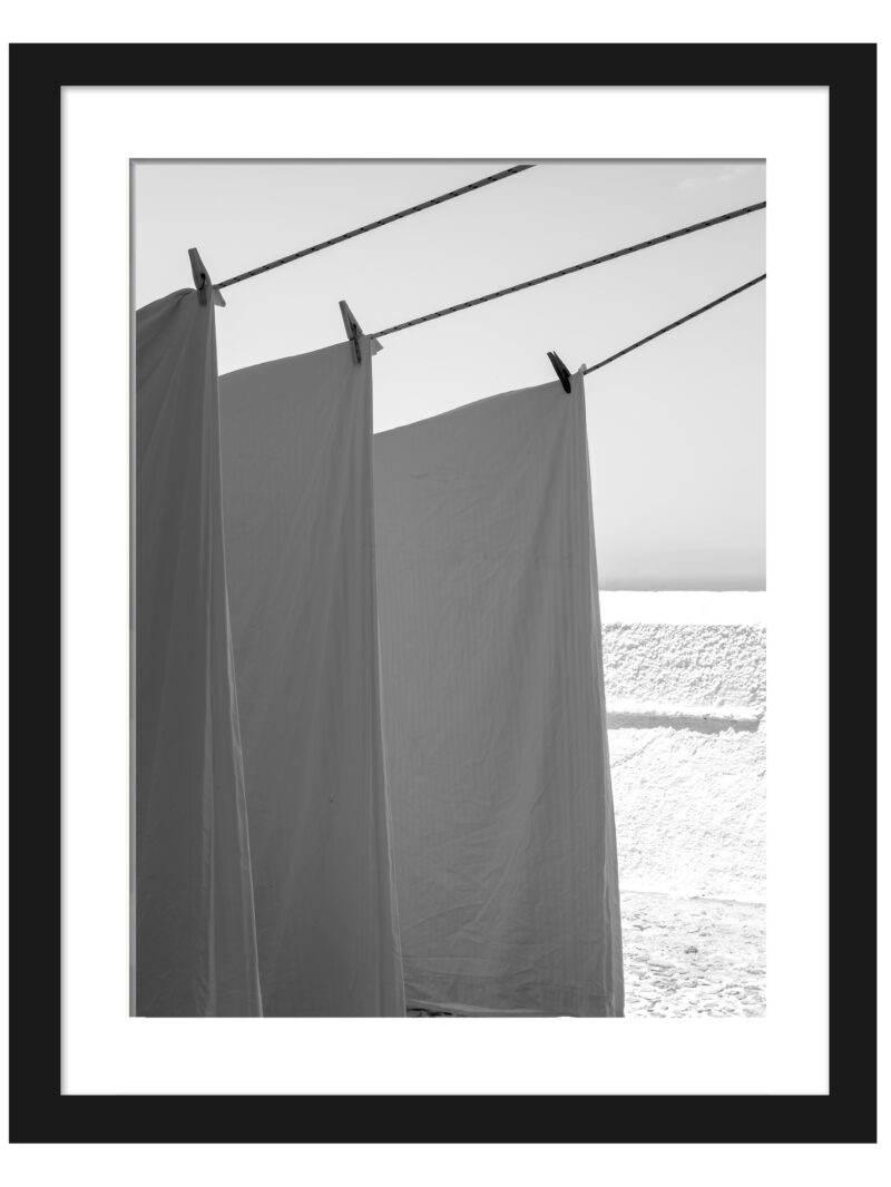 White sheets billowing in the wind resembling sails, set against a bright background in Fira, Santorini.