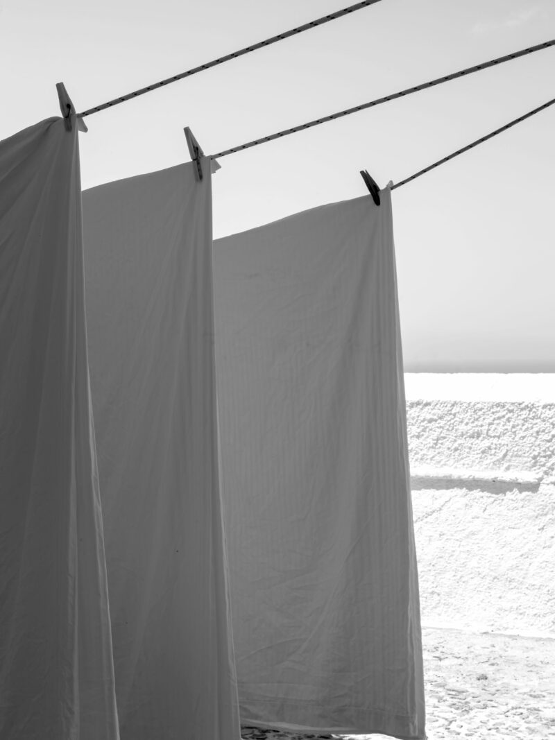 White sheets billowing in the wind resembling sails, set against a bright background in Fira, Santorini.