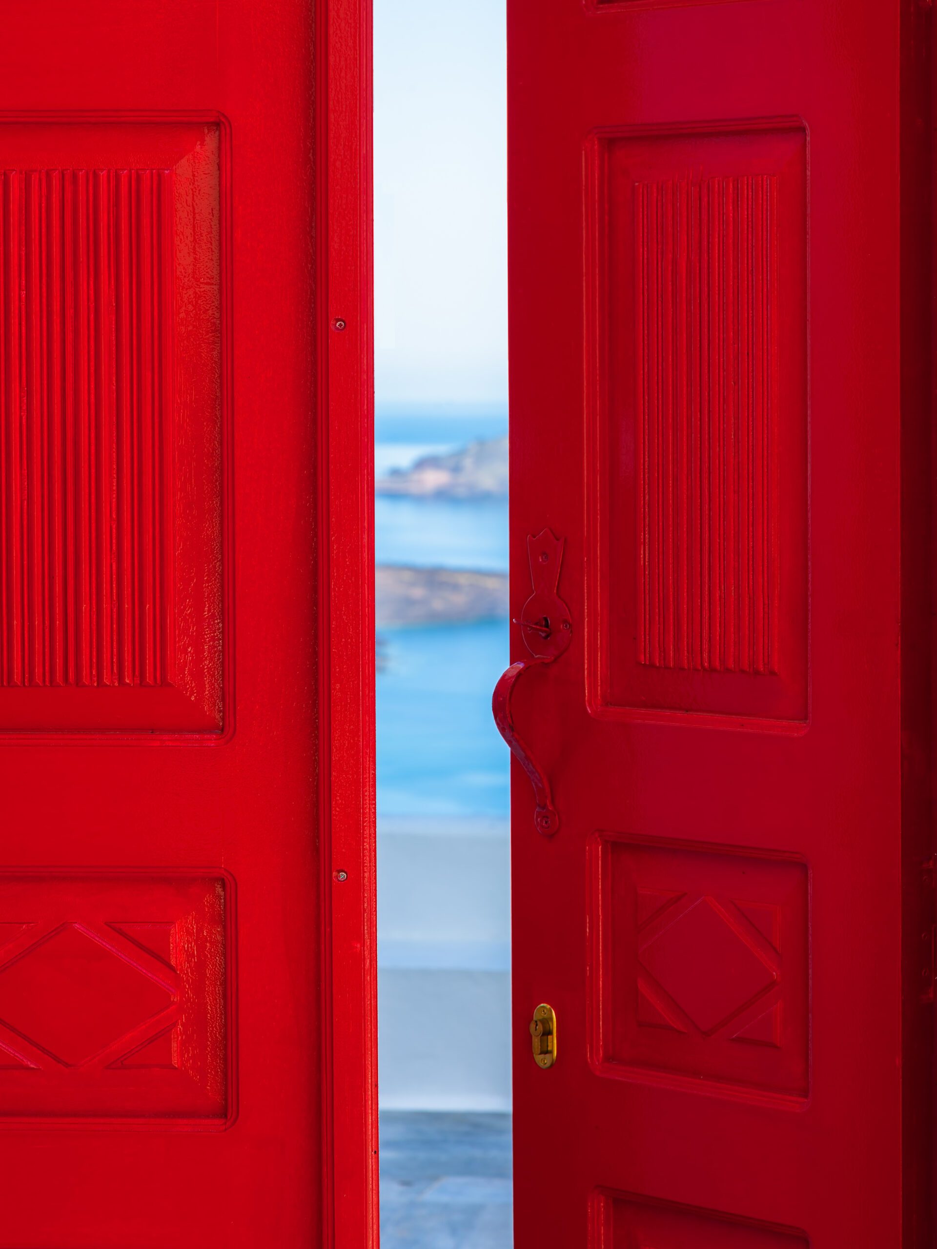 Bright red doorway opening to a view of the Santorini caldera with blue waters below.