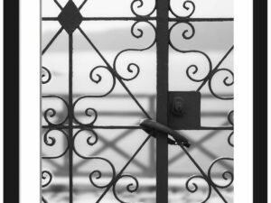 Black and white photo of an old iron gate in Fira, Santorini overlooking the sea.