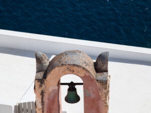 Ancient coral-colored bell against the dark blue ocean in Santorini, Greece.