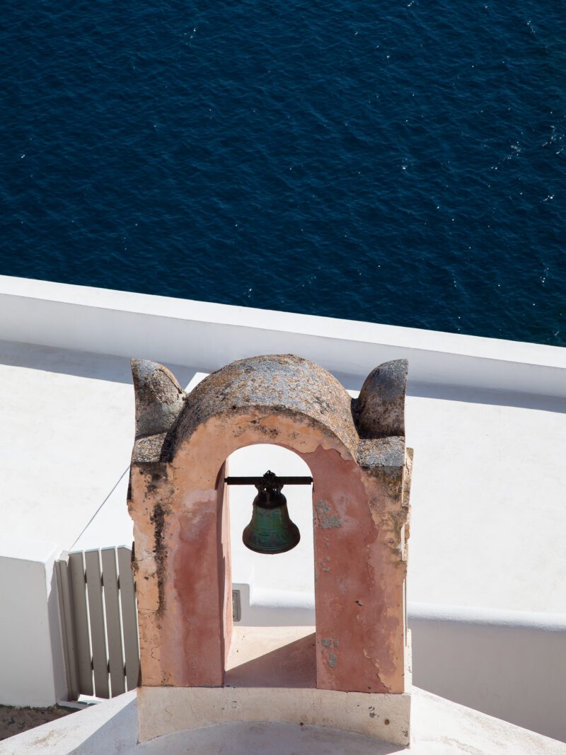Ancient coral-colored bell against the dark blue ocean in Santorini, Greece.