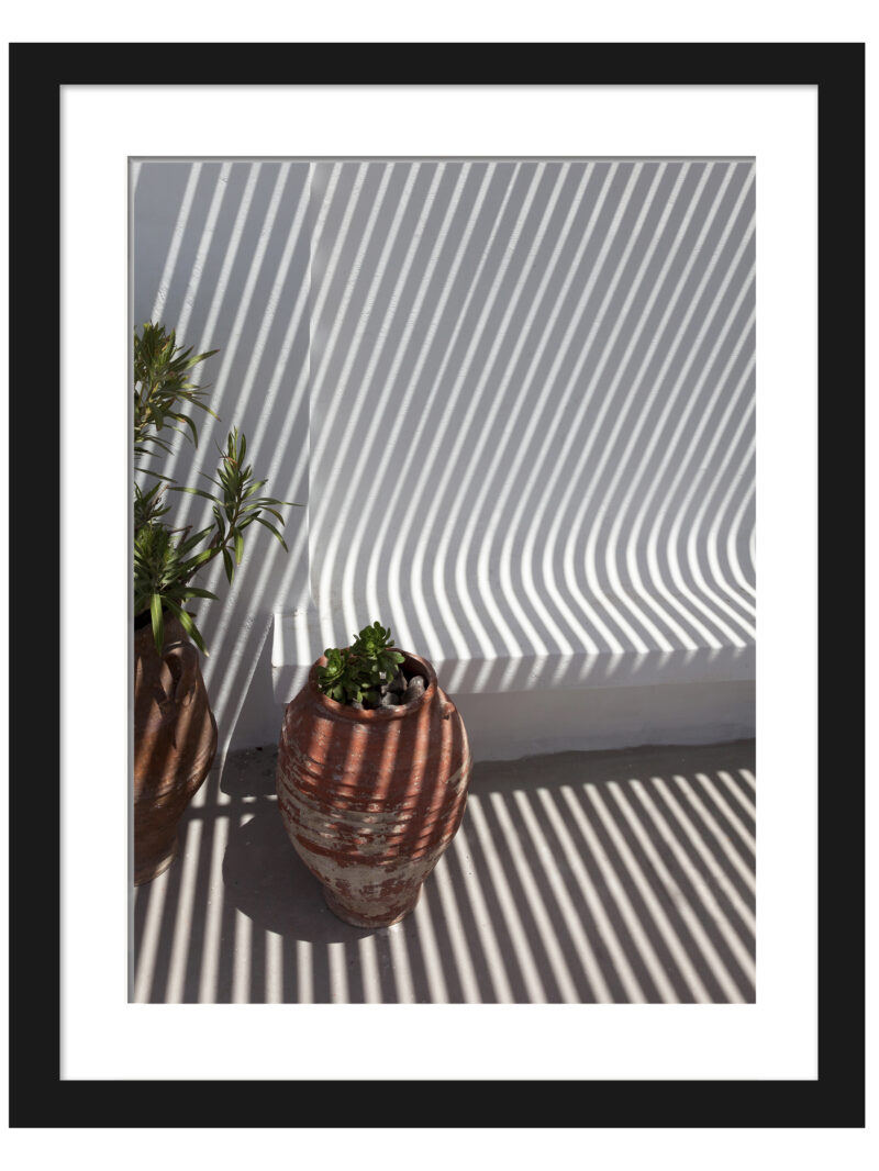 Clay pots on a Santorini balcony with dramatic geometric shadows cast by the sunlight.