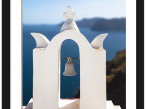 White bell tower with an angel sculpture on top, overlooking the deep blue sea in Santorini, Greece.