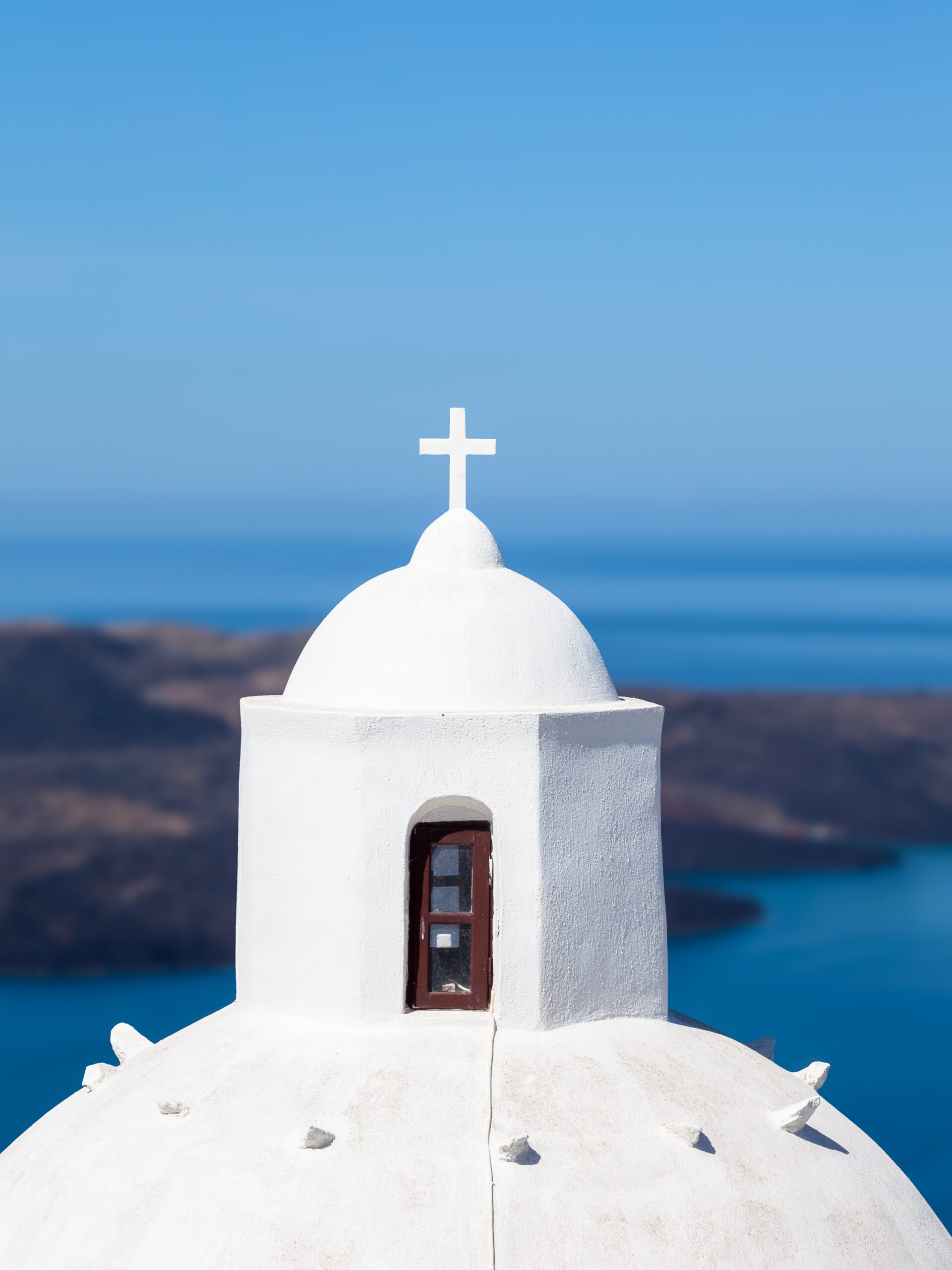White-domed church in Santorini with a clear view of the blue caldera.