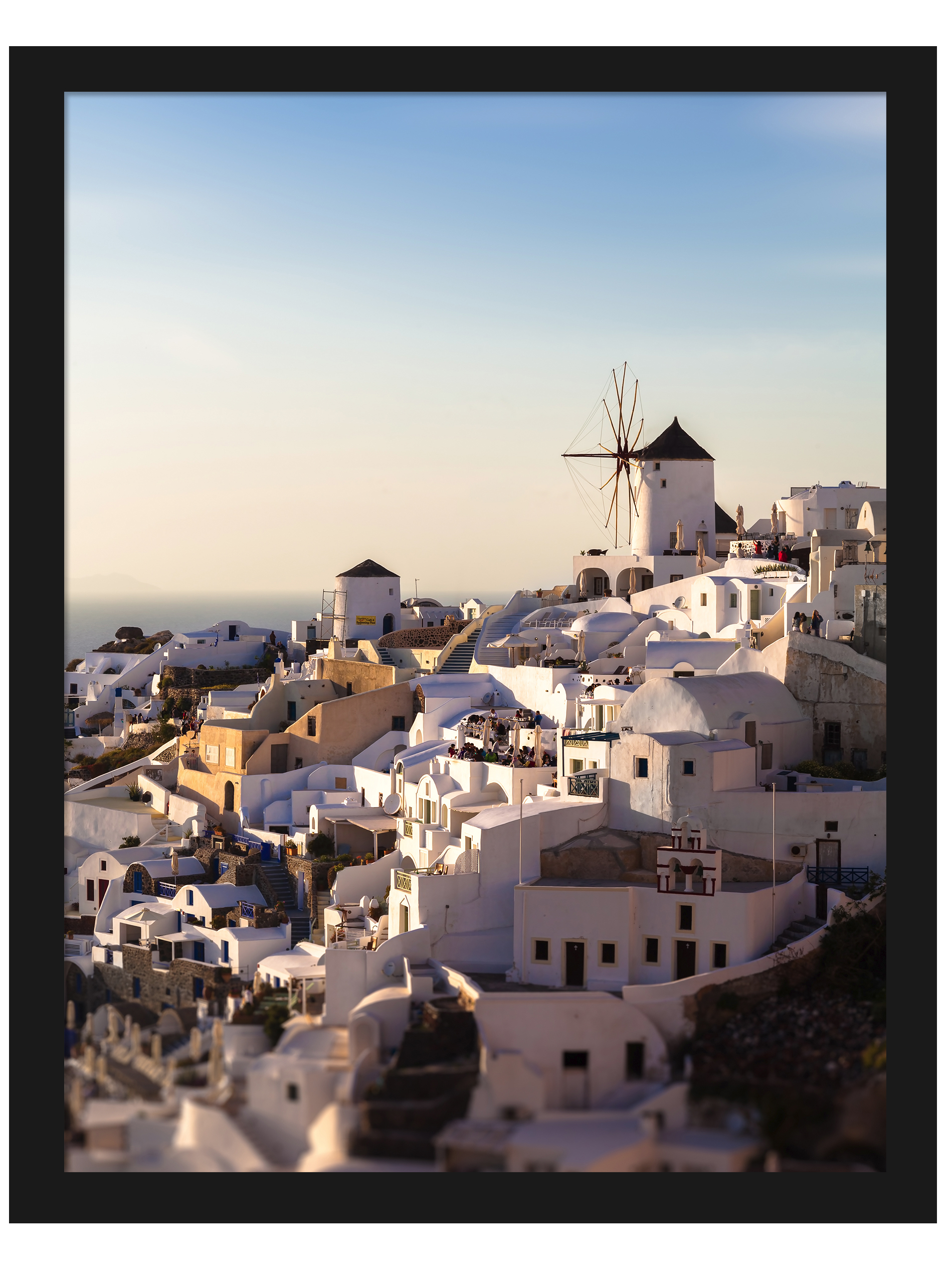 The village of Oia in Santorini, Greece, captured at dusk with soft golden lighting illuminating the iconic windmills and white buildings.