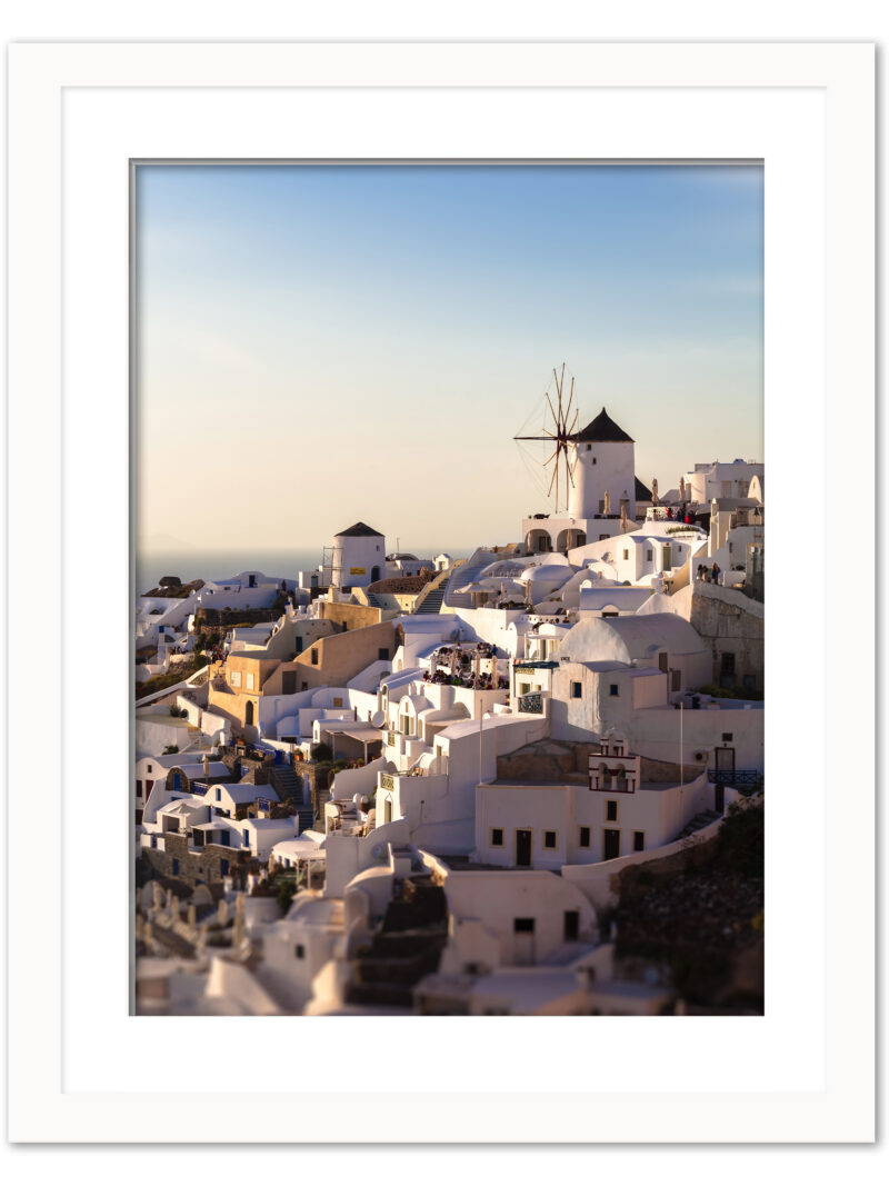 The village of Oia in Santorini, Greece, captured at dusk with soft golden lighting illuminating the iconic windmills and white buildings.