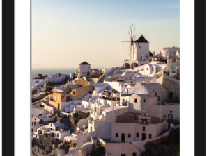 The village of Oia in Santorini, Greece, captured at dusk with soft golden lighting illuminating the iconic windmills and white buildings.