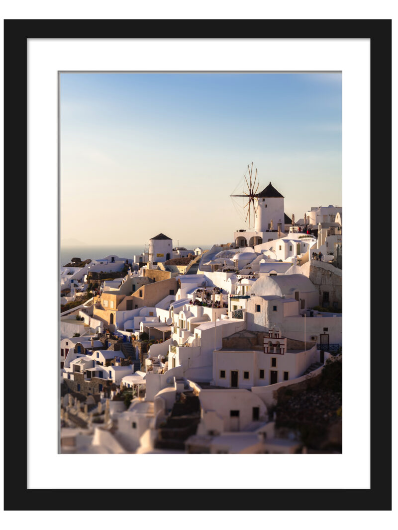 The village of Oia in Santorini, Greece, captured at dusk with soft golden lighting illuminating the iconic windmills and white buildings.