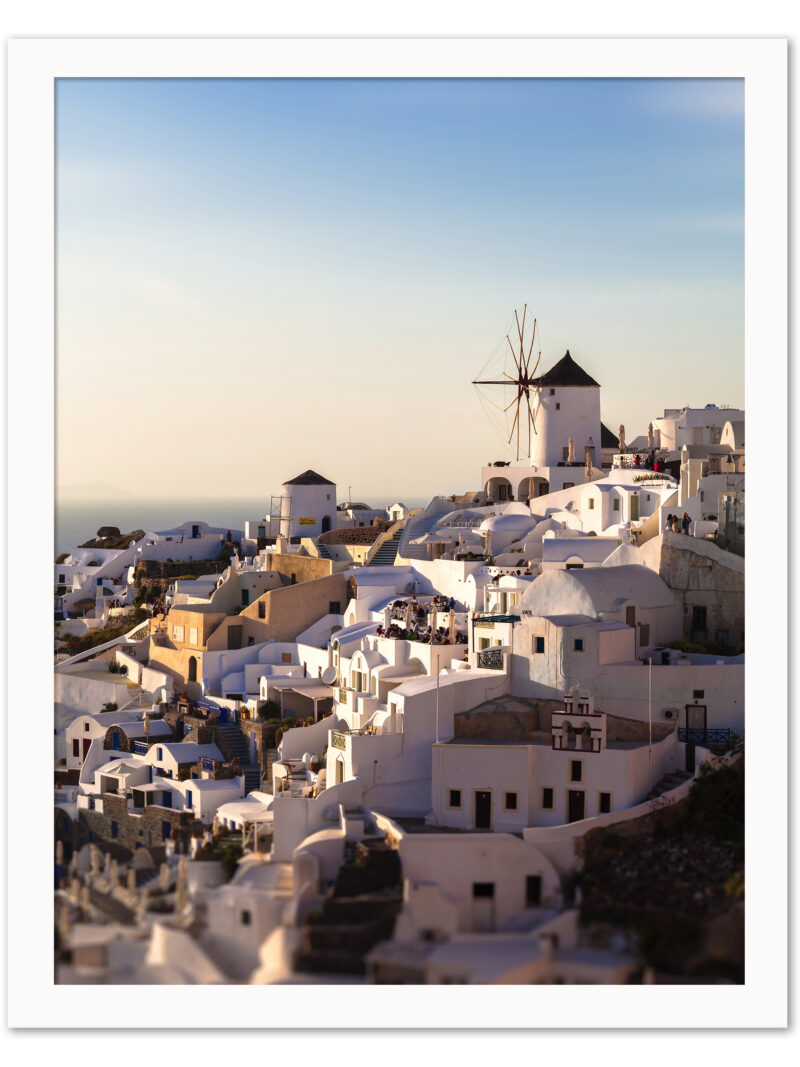 The village of Oia in Santorini, Greece, captured at dusk with soft golden lighting illuminating the iconic windmills and white buildings.