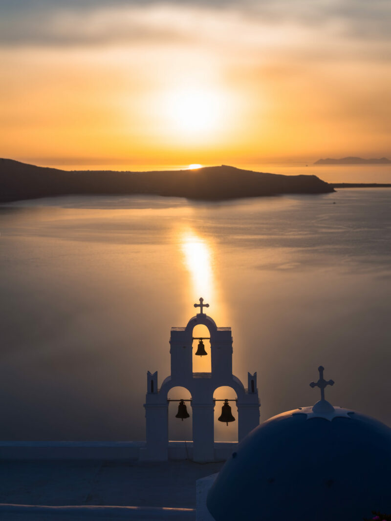 Church bells silhouette against a golden sunset in Santorini, Greece.