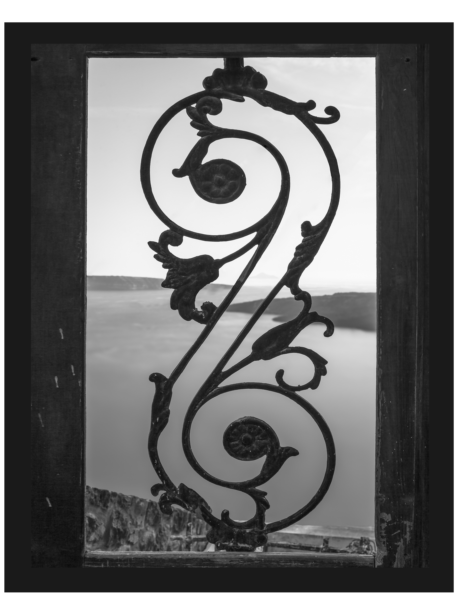 Black and white photo of an old iron gate with a view of the Santorini caldera.