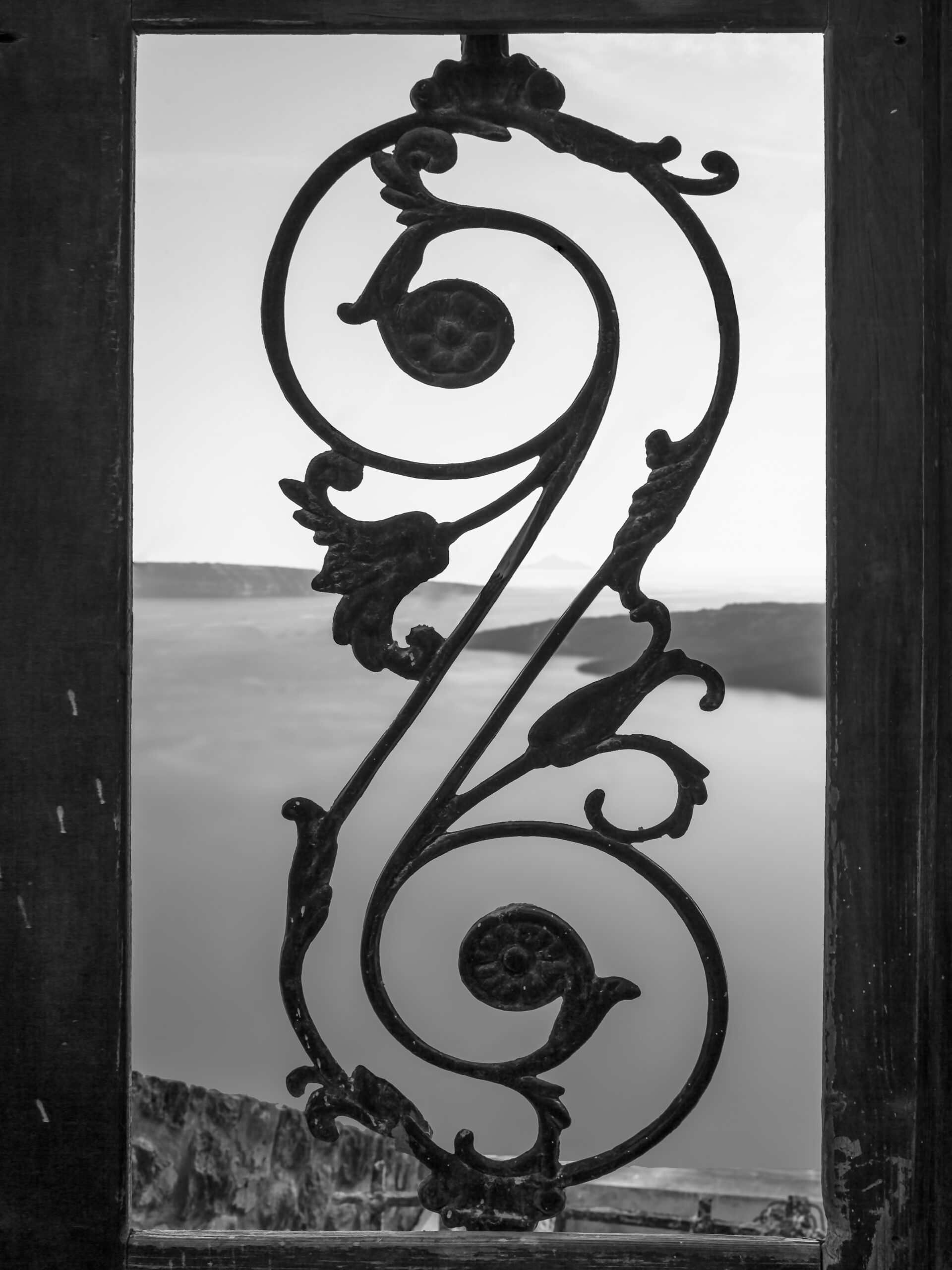 Black and white photo of an old iron gate with a view of the Santorini caldera.