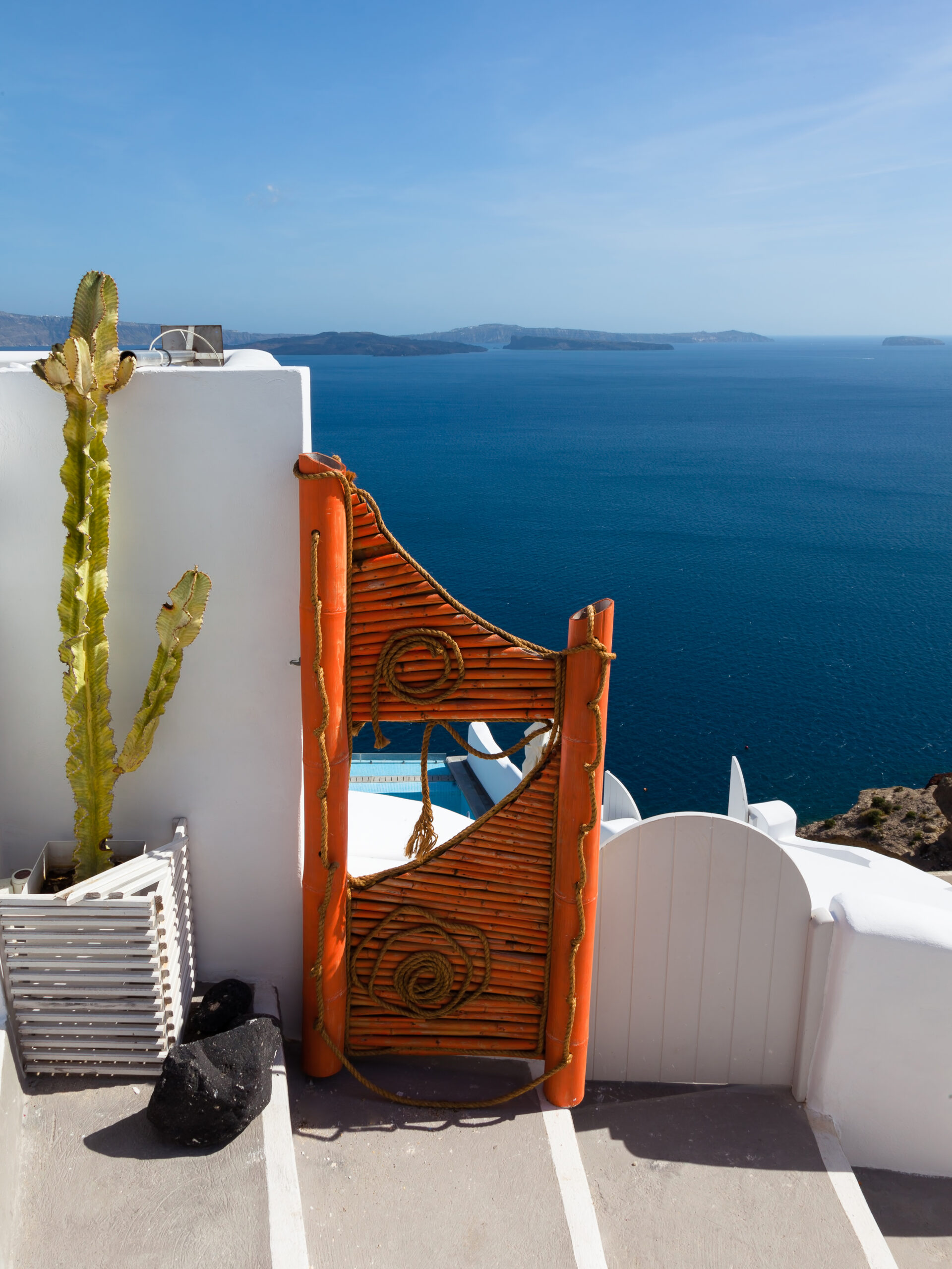 Vibrant orange gate in Fira, Santorini overlooking the clear blue caldera waters.