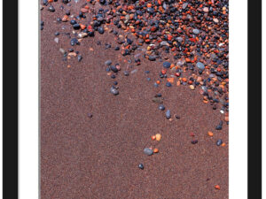Vibrant red sand and scattered colorful pebbles on a beach in Santorini, Greece.