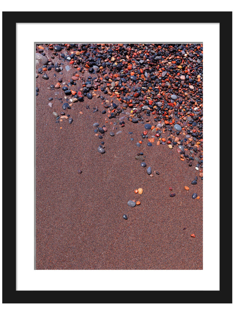 Vibrant red sand and scattered colorful pebbles on a beach in Santorini, Greece.