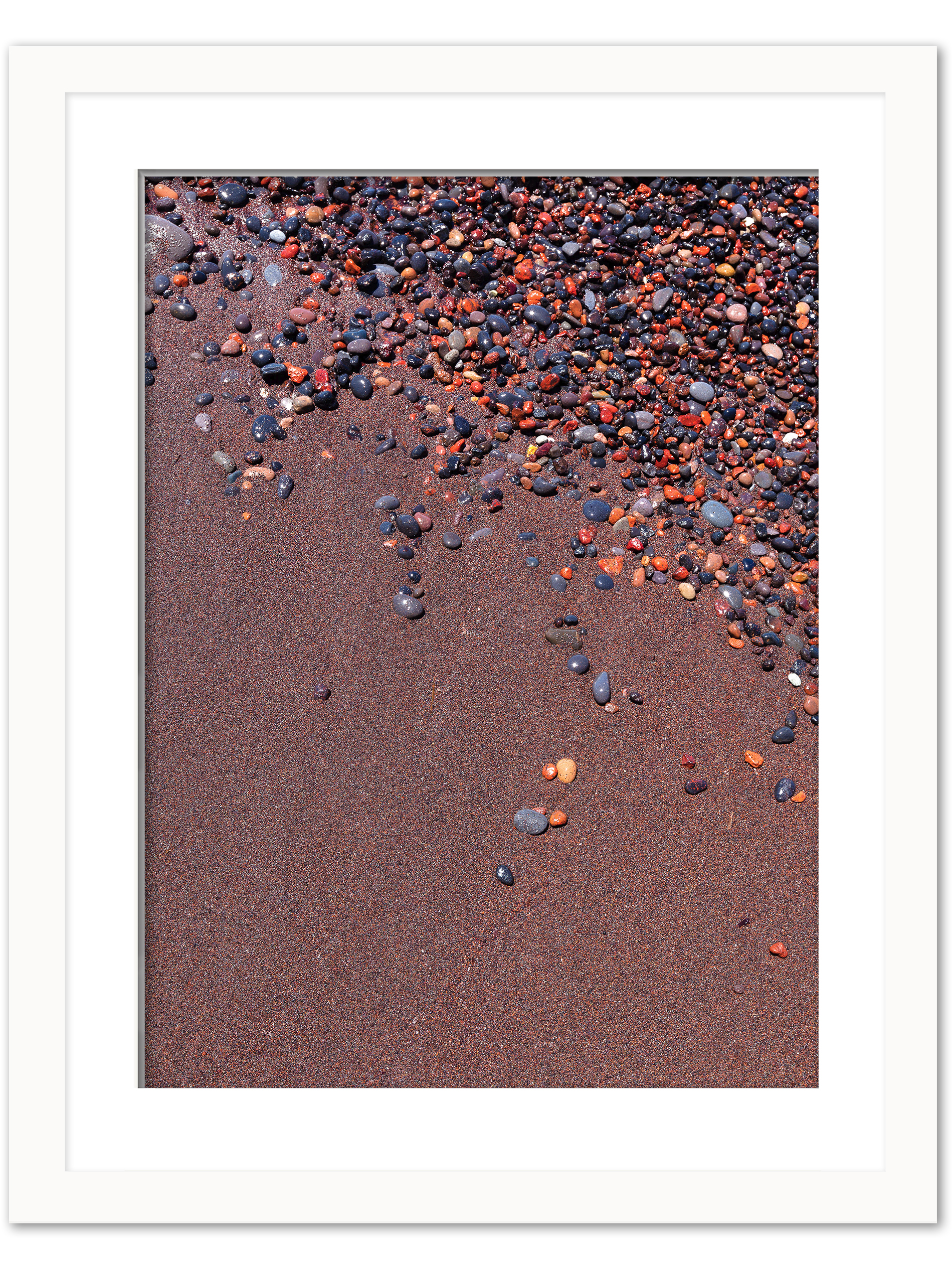 Vibrant red sand and scattered colorful pebbles on a beach in Santorini, Greece.