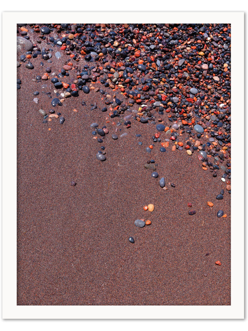 Vibrant red sand and scattered colorful pebbles on a beach in Santorini, Greece.