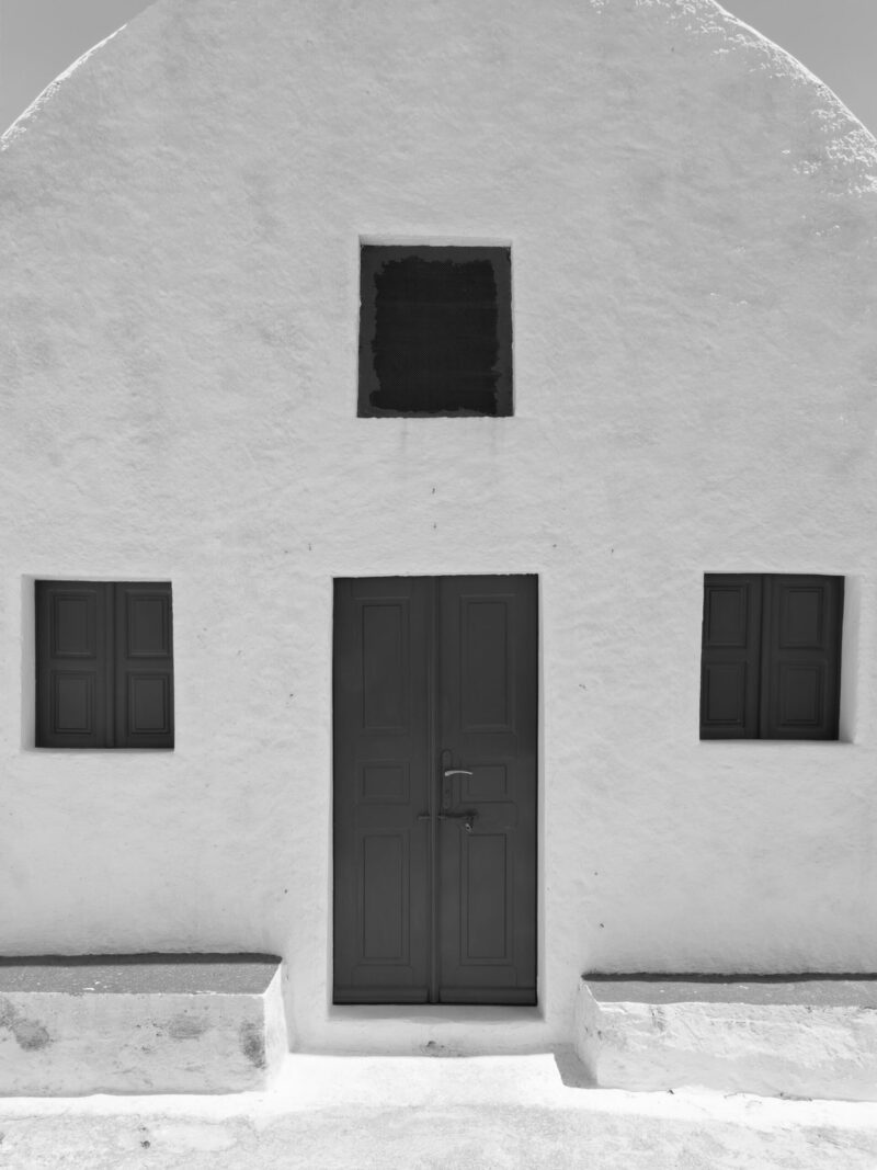 Simple white house in Santorini with symmetric windows and a minimalist design.