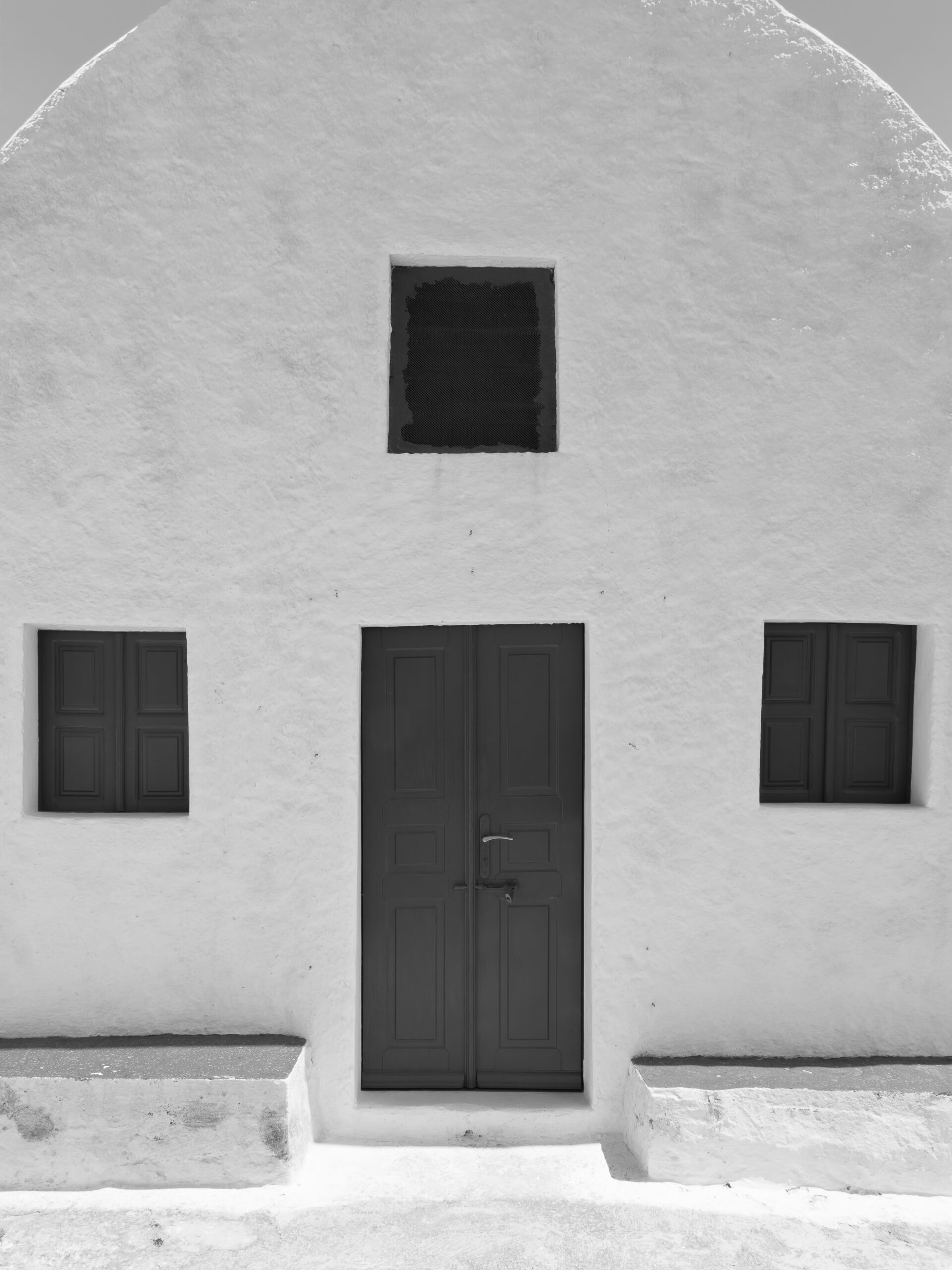 Simple white house in Santorini with symmetric windows and a minimalist design.