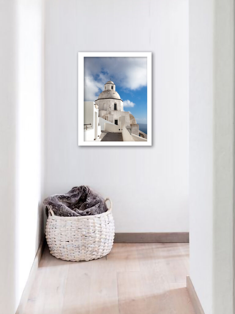 A scenic walkway in Fira, Santorini leading to a white domed church under a bright blue sky.