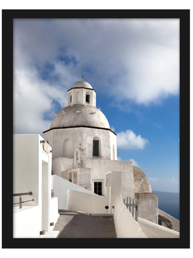 A scenic walkway in Fira, Santorini leading to a white domed church under a bright blue sky.