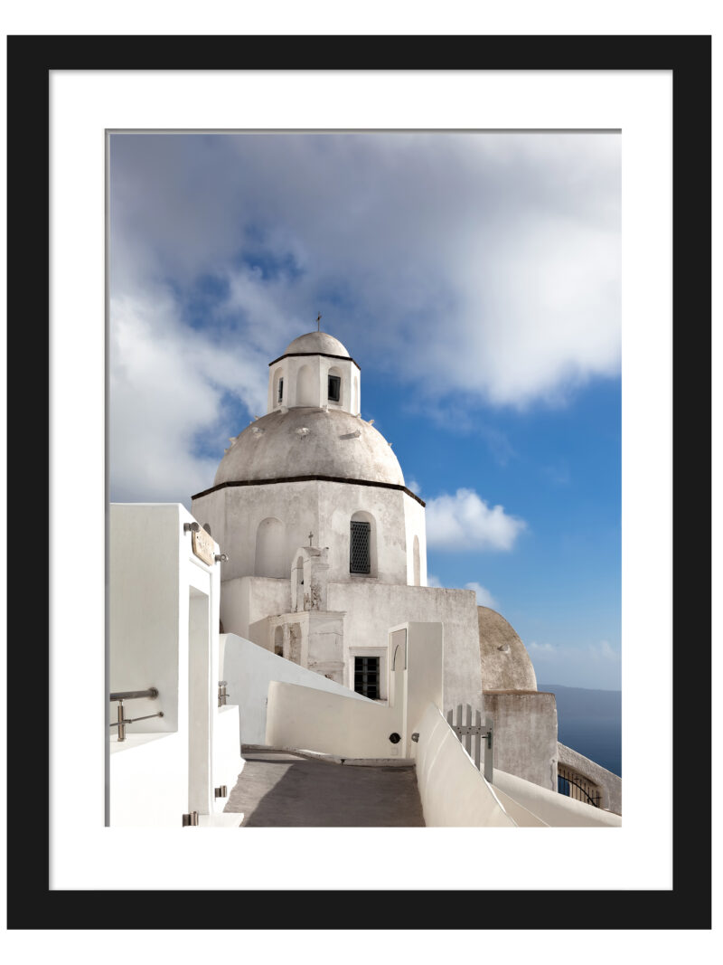 A scenic walkway in Fira, Santorini leading to a white domed church under a bright blue sky.