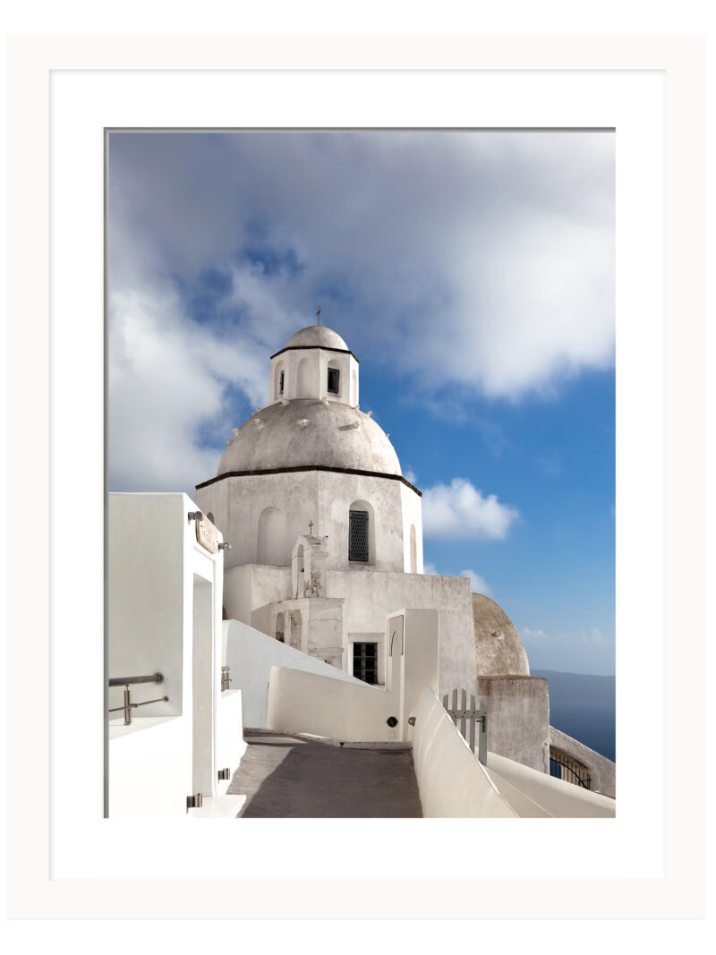 A scenic walkway in Fira, Santorini leading to a white domed church under a bright blue sky.