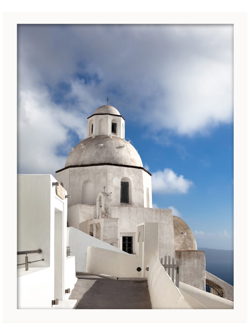 A scenic walkway in Fira, Santorini leading to a white domed church under a bright blue sky.